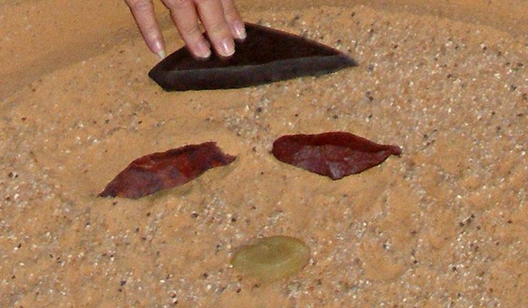 a small selection of the many high quality tools found in April 2008. (note: the red stones are actually much more geometrically precise—similar to the black stone being touched by the hand­—than they appear in this photo. unfortunately, they have been pushed slightly down into the sand, altering their true appearance)